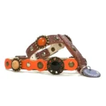 Brown and orange leather dog harness with posh stones in warm tones, brass studs, silver studs and a decorative enamel ornament, shown from the left side.