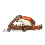 Dog harness in orange and brown leather featuring mixed‑metal studs, warm‑toned stones and an ornate enamel detail, shown from the right side.