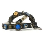 Black leather dog harness with ornate blue stones, brass and silver studs, a silver spike and decorative metal ornaments, shown from the left side.