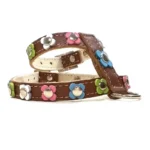Harnais en cuir brun décoré de petites fleurs pastel en rose, bleu, vert et blanc, chacune avec un rivet métallique central, vu du côté gauche.