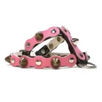 Black leather dog harness with a soft pink top layer, decorated with rounded and conical metal studs, shown from the left side. The layered leather and polished hardware create a bold yet cute look.