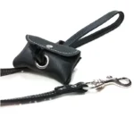Black leather poop bag holder attached to a leash with a waste bag pulled through the opening.