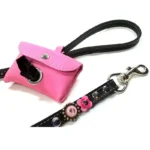 Pink leather poop bag holder attached to a leash with a waste bag pulled through the opening.